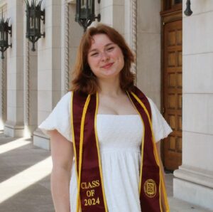 Charlotte smiles for a graduation portrait. She is wearing a white dress and a graduation stole.